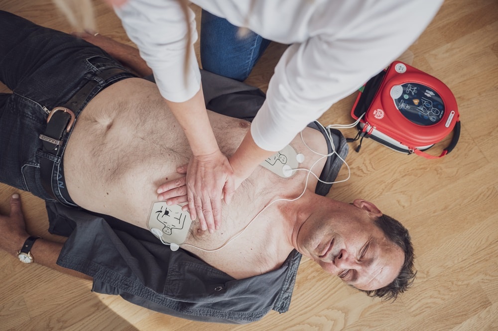 Mann wird mit Herzdruckmassage und Defibrillator wiederbelebt
