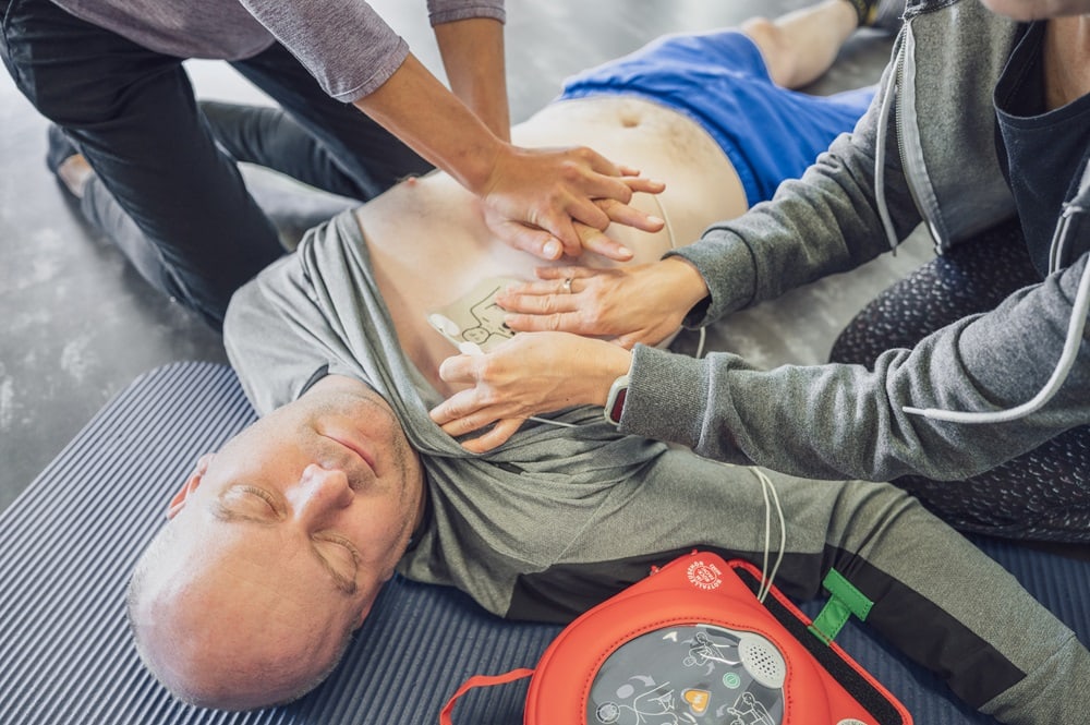 Mann beim Sport wird mit Herzdruckmassage und AED-Gerät wiederbelebt